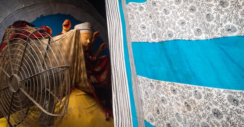 A vivid capture of a workshop scene in Kolkata, featuring vibrant fabrics and a fan.